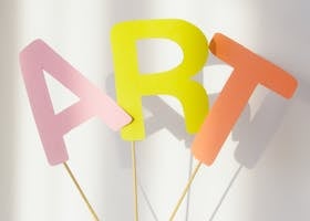 Colorful paper letters spelling 'ART' held in hand with bright lighting.